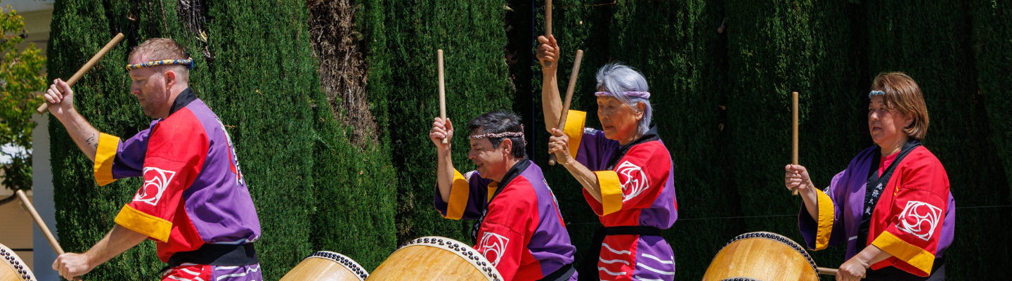 Four people in red and purple outfits playing drums.