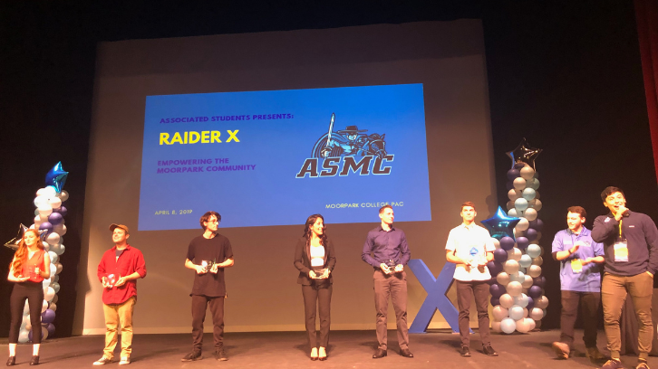 ASMC Board stands in from of screen with "Raider X" projected on it.