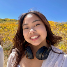 Arabella smiles for the photo while wearing headphones on her neck with a background of yellow flowers