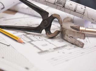 A hammer, a pencil, and other tools sitting on top of building blueprints.
