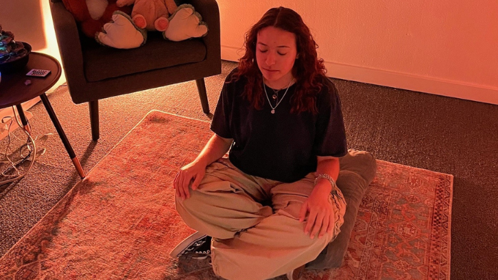 A student is shown meditating on a small cushion